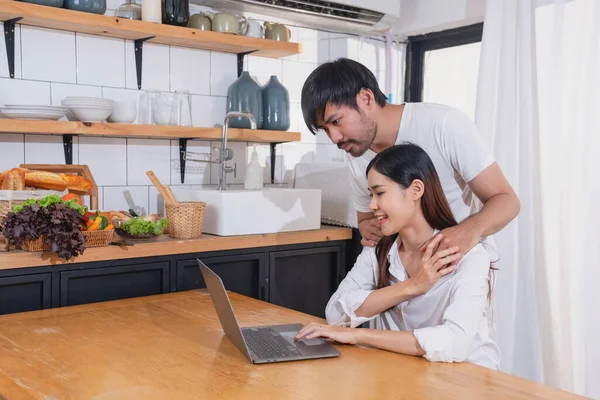 Meyve sebzelerle yemek yapan ve mutfakta dizüstü bilgisayar kullanan genç Asyalı çift aile içinde birlikte yemek pişiriyor. Aile kavramı..