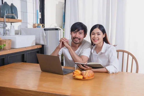 Meyve sebzelerle yemek yapan ve mutfakta dizüstü bilgisayar kullanan genç Asyalı çift aile içinde birlikte yemek pişiriyor. Aile kavramı..