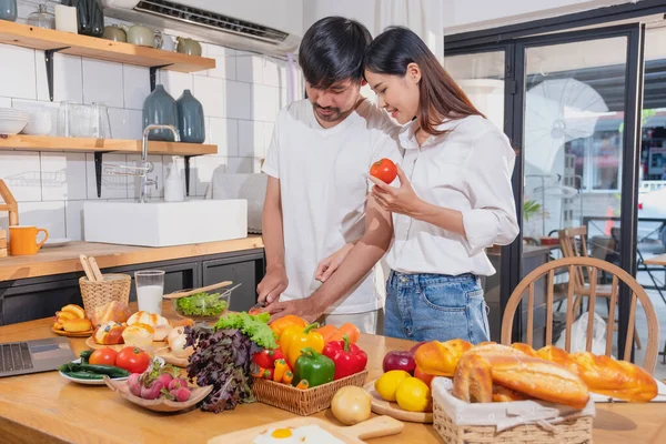 stock image Young Asian couple cooking with fruits and vegetables and using laptop in the kitchen To cook food together within the family happily, family concept.