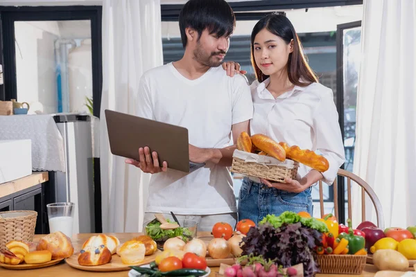 stock image Young Asian couple cooking with fruits and vegetables and using laptop in the kitchen To cook food together within the family happily, family concept.