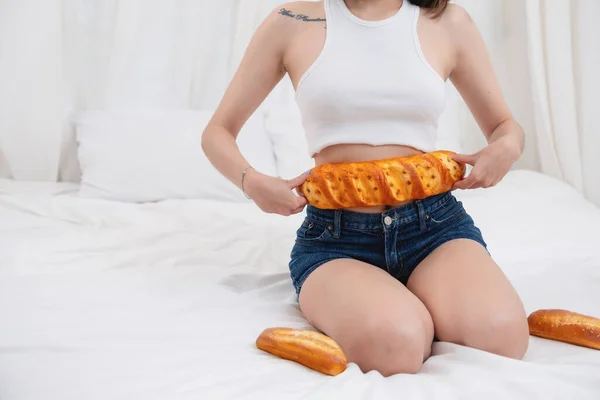 stock image Close-up shot of a white Asian woman with a tattoo sitting on the bed holding bread and eating junk food. without taking care of one's health to cause obesity, obesity concept.