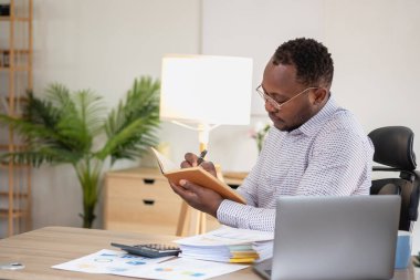 Afrikalı siyahi işadamı finansal rapor hazırlıyor ve yıllık kar analizi yapıyor. Şirketin mali durumunu kontrol eden bir muhasebeci şu anda ofiste..