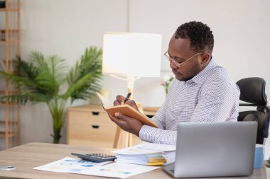 Afrikalı siyahi işadamı finansal rapor hazırlıyor ve yıllık kar analizi yapıyor. Şirketin mali durumunu kontrol eden bir muhasebeci şu anda ofiste..