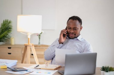 Afrikalı siyahi işadamları cep telefonlarının başında oturup müşterilerle iletişim kuruyor ve finansal raporlar hazırlıyor ve yıllık kâr analizlerini inceliyorlar. Bir muhasebeci şirketin mali durumunu kontrol eder..