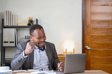 Akıllı telefon ve dizüstü bilgisayardan şirket sonuçlarını okurken Afro-Amerikalı siyahi adam mutlu oluyor. İş finans ve teknoloji kavramları.