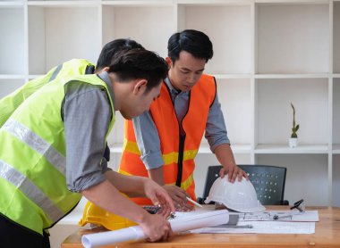Asyalı mühendisler maliyet tahminlerini belgelemek ve evler ve binalar için mimari ve mühendislik tasarımları için kat planları yazmak için beyin fırtınası yapıp ölçüm yapıyorlar..