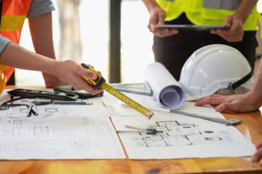 Asyalı mühendisler maliyet tahminlerini belgelemek ve evler ve binalar için mimari ve mühendislik tasarımları için kat planları yazmak için beyin fırtınası yapıp ölçüm yapıyorlar..