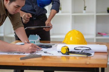 Asyalı mühendisler maliyet tahminlerini belgelemek ve evler ve binalar için mimari ve mühendislik tasarımları için kat planları yazmak için beyin fırtınası yapıp ölçüm yapıyorlar..