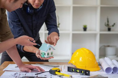 Asyalı mühendisler maliyet tahminlerini belgelemek ve evler ve binalar için mimari ve mühendislik tasarımları için kat planları yazmak için beyin fırtınası yapıp ölçüm yapıyorlar..