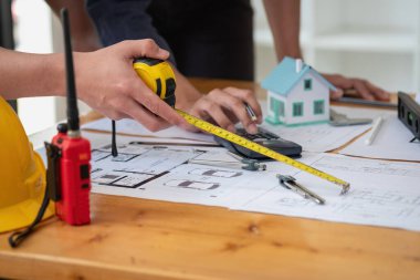 Asyalı mühendisler maliyet tahminlerini belgelemek ve evler ve binalar için mimari ve mühendislik tasarımları için kat planları yazmak için beyin fırtınası yapıp ölçüm yapıyorlar..