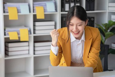 Sarı takım elbiseli genç Asyalı iş kadını dizüstü bilgisayar ve akıllı telefonla iş arkadaşlarına belli hedefleri olan bir şirket projesini başardıkları için neşe veriyor. Başarı kavramı..