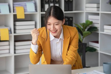 Sarı takım elbiseli genç Asyalı iş kadını dizüstü bilgisayar ve akıllı telefonla iş arkadaşlarına belli hedefleri olan bir şirket projesini başardıkları için neşe veriyor. Başarı kavramı..