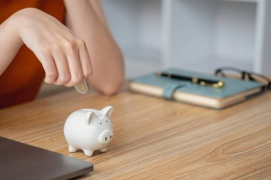 Genç Asyalı kadın emeklilik için para biriktiriyordu. Kumbaradan para biriktiriyordu ve defter, tasarruf konsepti gibi notlar alıyordu..