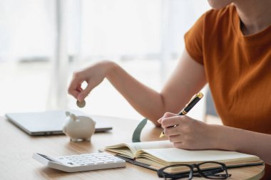 Genç Asyalı kadın emeklilik için para biriktiriyordu. Kumbaradan para biriktiriyordu ve defter, tasarruf konsepti gibi notlar alıyordu..