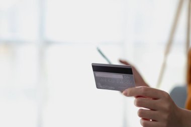 Kredi kartı ve akıllı telefon tutan genç Asyalı kadın tüketici evde yerde oturmuş online bankacılık işlemlerini yapıyor. E-ticaret sanal alışveriş, güvenli mobil bankacılık kavramı.