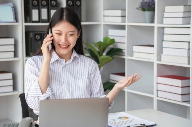 Asyalı iş kadını telefonda konuşuyor. Modern ofiste müşterilerle konuşuyor. Ofiste yeni bir iş yapma şekli için..
