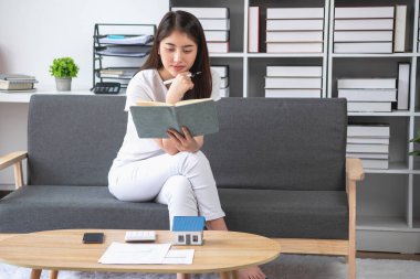 rahat bir koltukta oturan ve planlayan bir kadın hesap makinesi ve ev, masa, sigorta ve konut, kredi ve ikamet bütçesi, iş ve mülkiyet konseptiyle gider ve ipotek hesapları yapar..