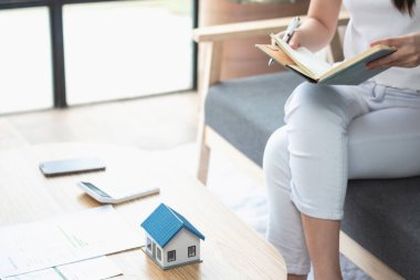 rahat bir koltukta oturan ve planlayan bir kadın hesap makinesi ve ev, masa, sigorta ve konut, kredi ve ikamet bütçesi, iş ve mülkiyet konseptiyle gider ve ipotek hesapları yapar..