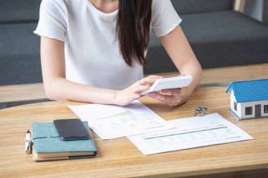 rahat bir koltukta oturan ve planlayan bir kadın hesap makinesi ve ev, masa, sigorta ve konut, kredi ve ikamet bütçesi, iş ve mülkiyet konseptiyle gider ve ipotek hesapları yapar..