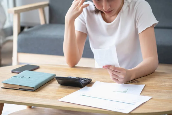 Young Asian woman sitting and calculating expenses and mortgage with calculator and house on table Worried about payments and non-repayable loans, business, and property.