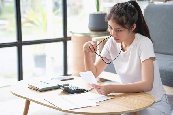 Young Asian woman sitting and calculating expenses and mortgage with calculator and house on table Worried about payments and non-repayable loans, business, and property.