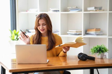 Mutlu Latin kız kolej öğrencisi uzaktan öğrenim kursu, uzak üniversite web sitesi ya da laptop üzerinden konuşma videosu alıyor ve evdeki ya da kampüsteki sanal toplantı seminerinde not defteri kullanıyor.