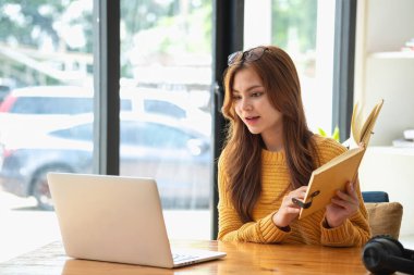 Mutlu Latin kız kolej öğrencisi uzaktan öğrenim kursu, uzak üniversite web sitesi ya da laptop üzerinden konuşma videosu alıyor ve evdeki ya da kampüsteki sanal toplantı seminerinde not defteri kullanıyor.