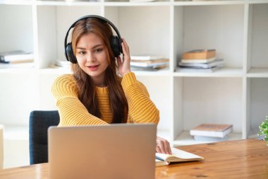 Mutlu Latin kız kolej öğrencisi uzaktan öğrenim kursu, uzak üniversite web sitesi ya da laptop üzerinden konuşma videosu alıyor ve evdeki ya da kampüsteki sanal toplantı seminerinde not defteri kullanıyor.