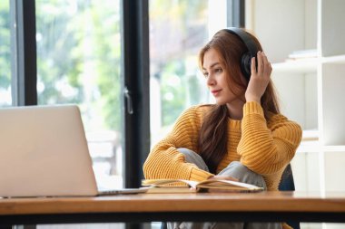 Mutlu Latin kız kolej öğrencisi uzaktan öğrenim kursu, uzak üniversite web sitesi ya da laptop üzerinden konuşma videosu alıyor ve evdeki ya da kampüsteki sanal toplantı seminerinde not defteri kullanıyor.