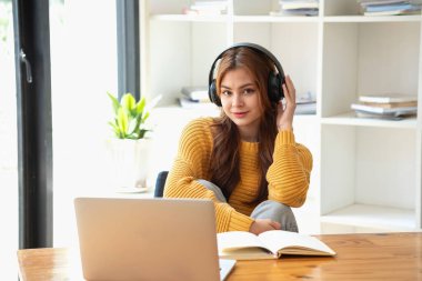 Mutlu Latin kız kolej öğrencisi uzaktan öğrenim kursu, uzak üniversite web sitesi ya da laptop üzerinden konuşma videosu alıyor ve evdeki ya da kampüsteki sanal toplantı seminerinde not defteri kullanıyor.