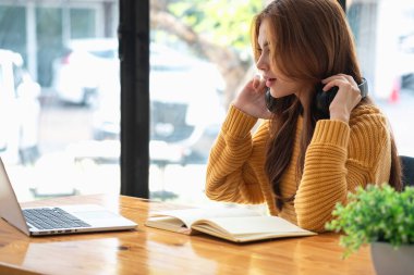 Mutlu Latin kız kolej öğrencisi uzaktan öğrenim kursu, uzak üniversite web sitesi ya da laptop üzerinden konuşma videosu alıyor ve evdeki ya da kampüsteki sanal toplantı seminerinde not defteri kullanıyor.