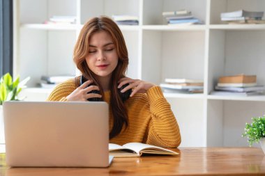 Mutlu Latin kız kolej öğrencisi uzaktan öğrenim kursu, uzak üniversite web sitesi ya da laptop üzerinden konuşma videosu alıyor ve evdeki ya da kampüsteki sanal toplantı seminerinde not defteri kullanıyor.