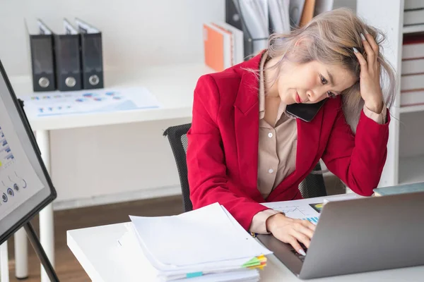 stock image Busy businesswoman at work and talking on the phone looking at laptop screen Frustrated young woman arguing with customer holding a smartphone and being stressed solve business problems.