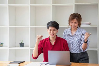 Ofiste dizüstü bilgisayar kullanan neşeli iş adamları. Modern bir çalışma alanında birlikte çalışırken gülümseyen genç girişimciler. İki genç iş adamı bir masada birlikte oturuyorlar..