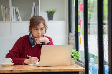 Bilgisayarlı, mikrofonlu kulaklık takan Asyalı güzel iş kadını dizüstü bilgisayara bakıyor müşterileri internetten eğiten mutlu iş kadını..