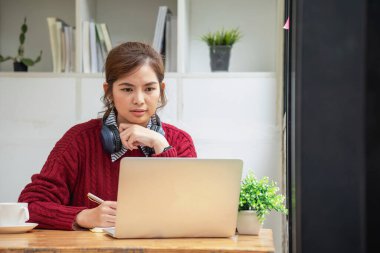 Bilgisayarlı, mikrofonlu kulaklık takan Asyalı güzel iş kadını dizüstü bilgisayara bakıyor müşterileri internetten eğiten mutlu iş kadını..