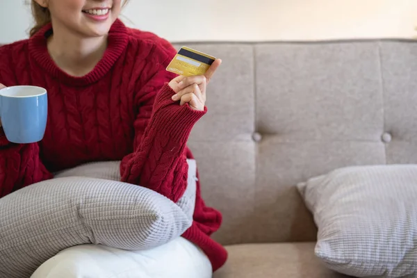 A young Asian woman with a happy smile holds a credit card and uses a smartphone to shop online Online payment concept.