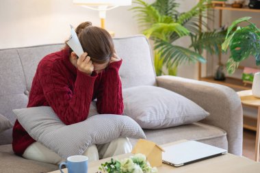 Genç bir Asyalı kadın evindeki bir kanepede oturuyor, aylık giderleri hakkında endişeli ve hayal kırıklığına uğramış hissediyor. Çeşitli faturalar..