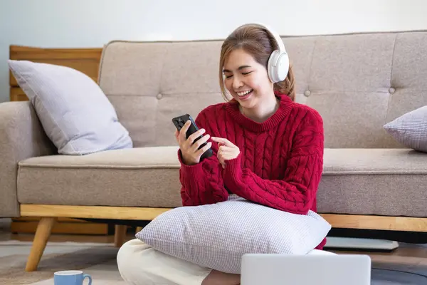 Kırmızı gündelik elbiseli güzel bir kadın evde kanepede dinlenirken müzik dinlemekten ve gülümsemekten zevk alıyor. Kulaklıklı genç bir kadın evde dizüstü bilgisayar ve akıllı telefon kullanıyor. Rahatla konsept.