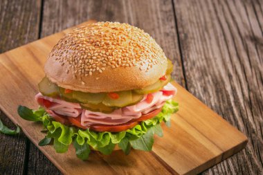 Sosisli sandviç, salatalık, domates ve ahşap zemin üzerinde marul yaprakları.