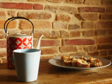 Bir çaydanlık, bir fincan ve ahşap çekmecede dilimlenmiş bir tabak ekmek.