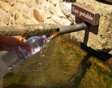 Plastik bir şişeyi tutan ve pınardan içme suyu dolduran bir elin yakın plan çekimi.