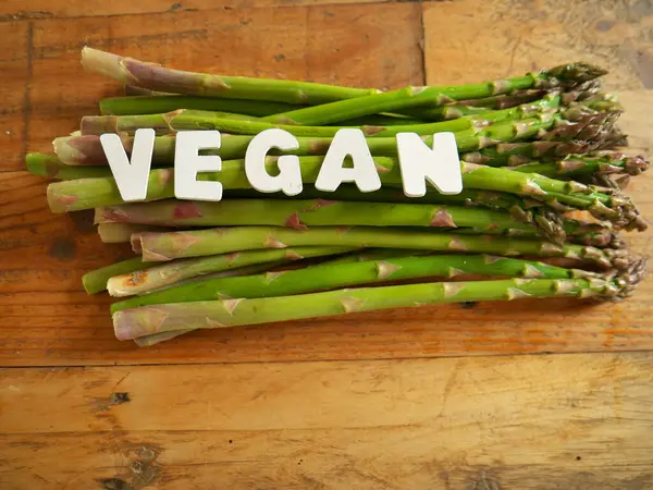 VEGAN harflerinin yakın plan fotoğrafı tahtadan kahverengi masa ve alttaki kuşkonmaz..