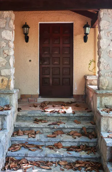 Kuru yapraklarla kaplı taş basamaklar evin ön kapısına çıkıyor..