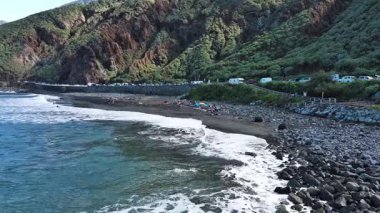 A breathtaking coastline with waves crashing on rocky shores, set against lush mountains in the background.
