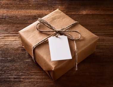 Kırsal ahşap masada boş etiketli kahverengi Noel hediyesi kutusu.