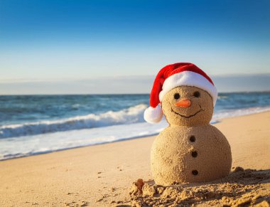 Güneşli bir sahilde Noel Baba şapkalı kum adam.