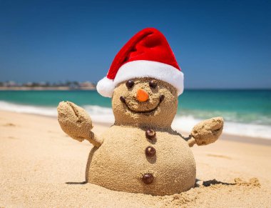 Güneşli bir sahilde Noel Baba şapkalı kum adam.