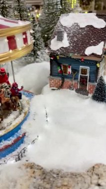 Seramik heykelciklerden oluşan bir köyün Noel sahnesi, bir atlıkarınca, dekore edilmiş evler, komik kar küremeli vatandaşlar, ve büyük bir Noel ağacı, 4k, gerçek.