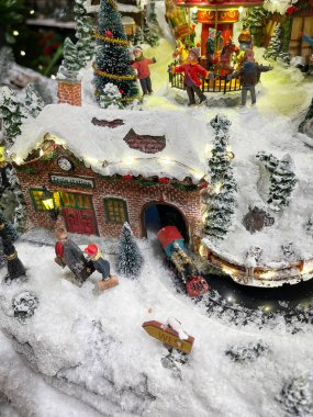 Tren istasyonunda bekleyen iki kişinin minyatür Noel sahnesi tünelden çıkan bir tren ve insanların Noel 'i bir atlıkarıncayla kutladıkları bir panayır.